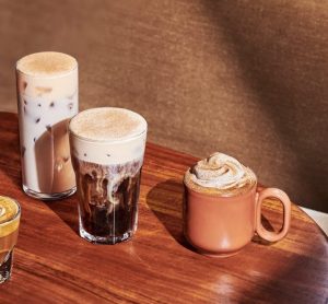 Two Starbucks autumn drinks, a Pumpkin Spice Latte and a Pecan Oatmilk Cortado, sitting side by side on a wooden coffee table.