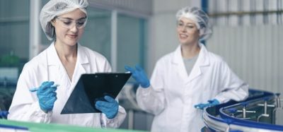 Two food safety specialists in white labcoats reviewing a checklist on a clipboard in a food production facility, representing ISO 22000 standard compliance.