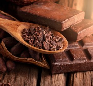 Cocoa beans and a cocoa pod on a wooden surface, representing the source of chocolate and the challenges in sustainable cocoa farming.