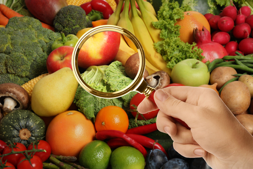 Fresh fruits and vegetables under a magnifying glass, symbolising scrutiny and inspection in global food supply chains.
