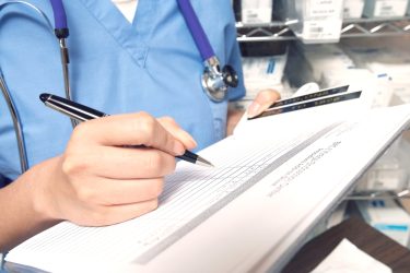 A close-up of a female nurse writing on the patient's medical chart.